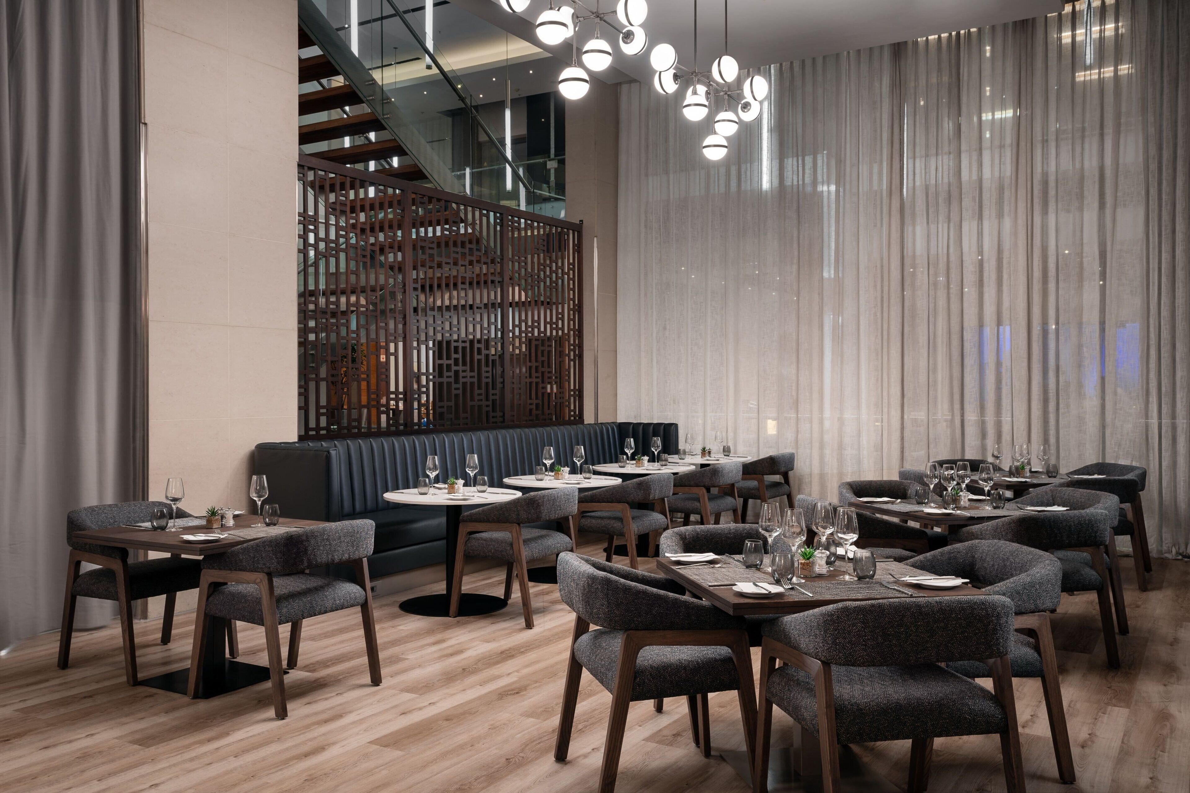 A modern dining area with multiple tables and chairs, a staircase, and a decorative partition.
