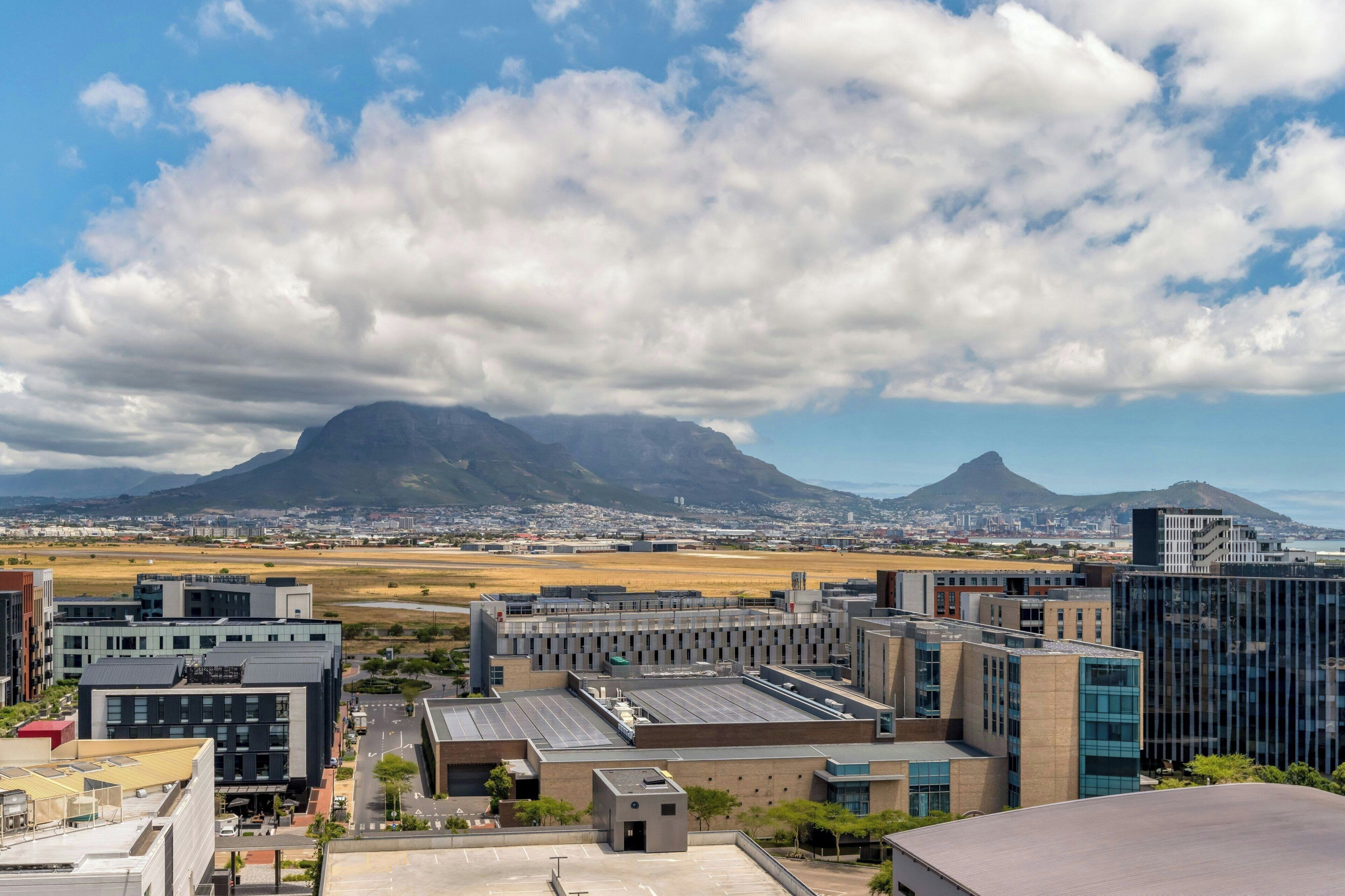 A modern building complex with a flat roof, surrounded by open fields and mountains in the background.