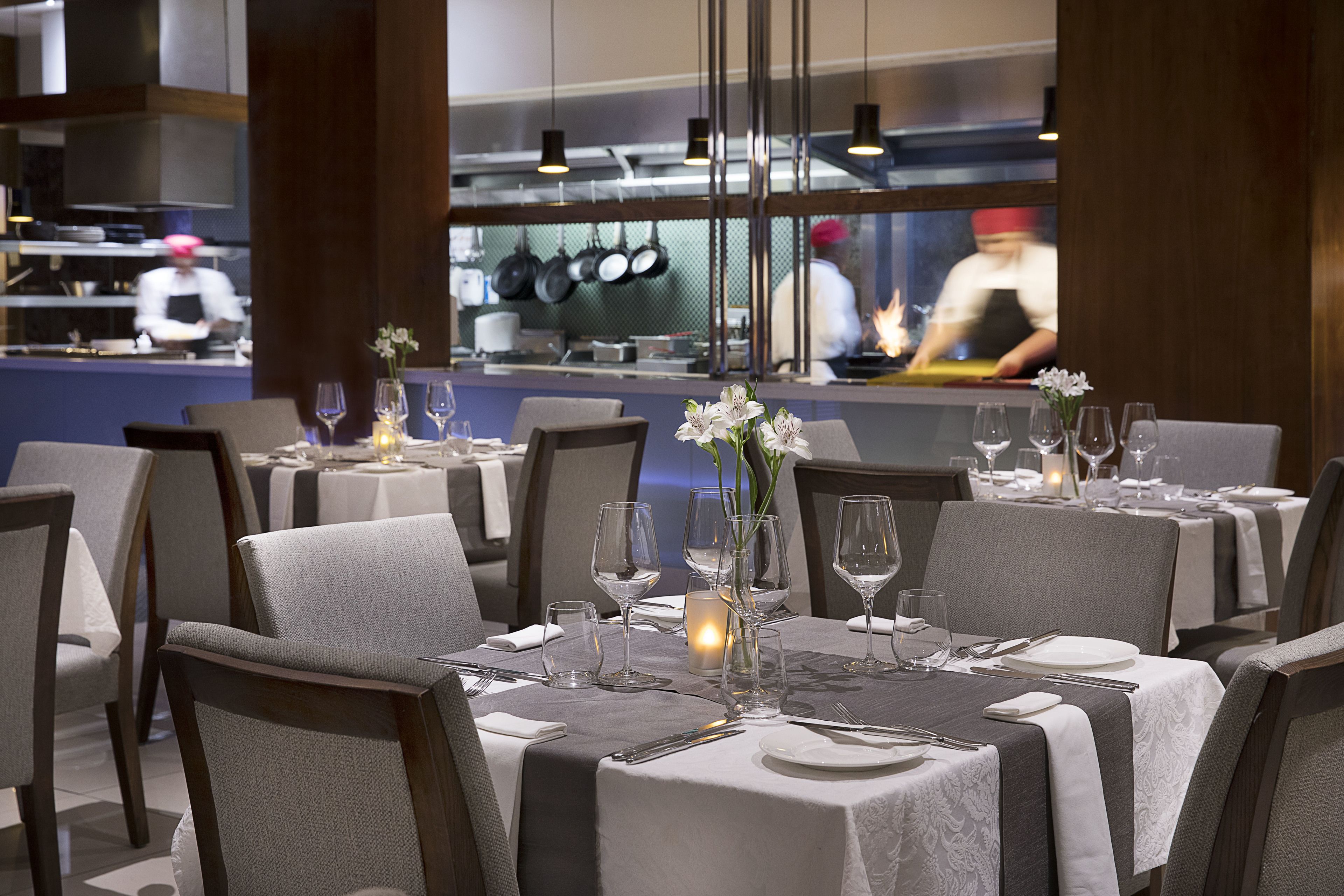 Un restaurante con mesas dispuestas para comer, vistas a la cocina y una vela sobre la mesa.