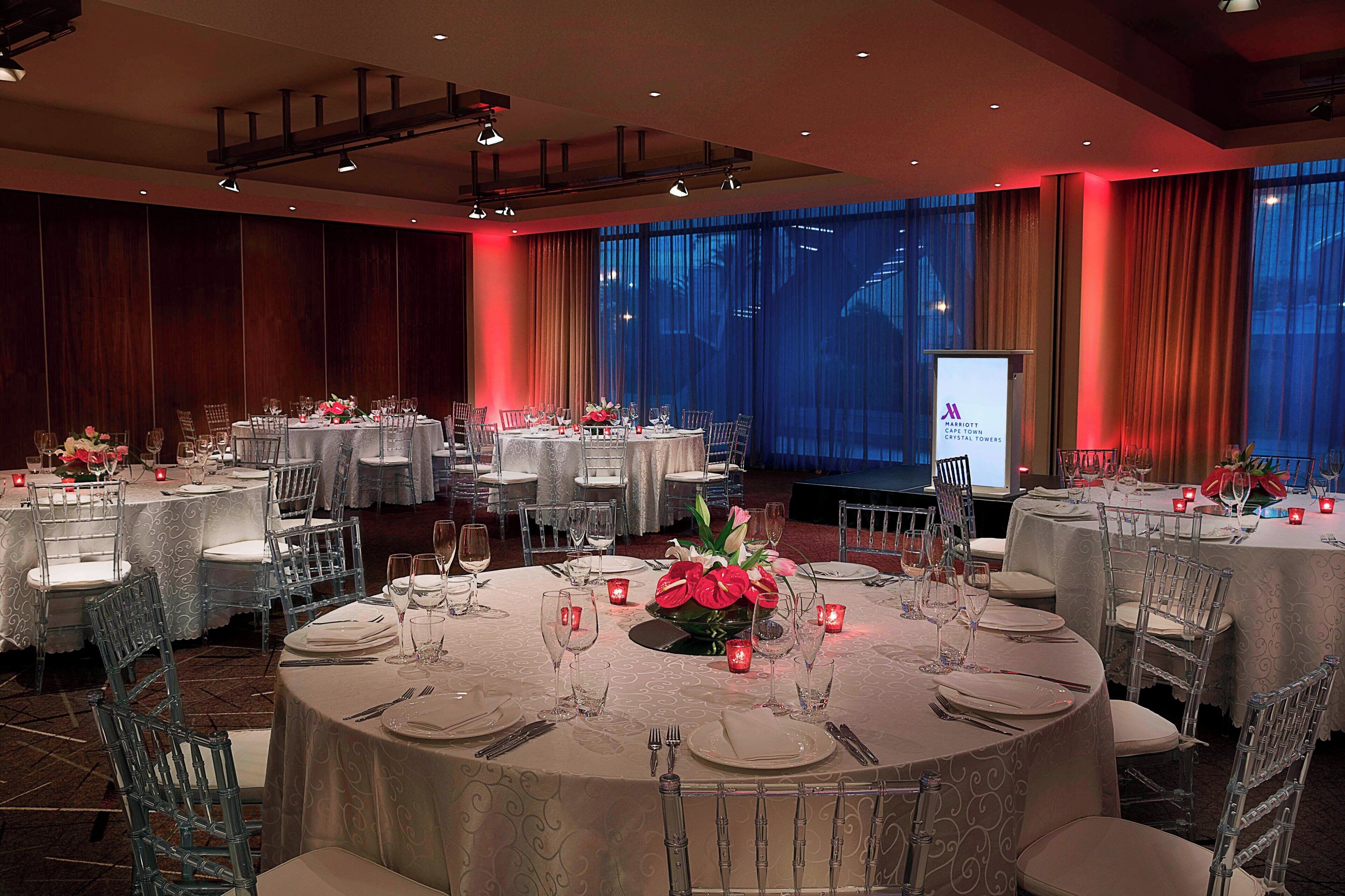 A banquet hall with round tables set for dining, featuring clear chairs and white tablecloths.