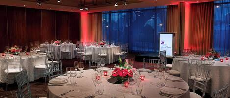 A banquet hall with round tables set for dining, featuring clear chairs and white tablecloths.