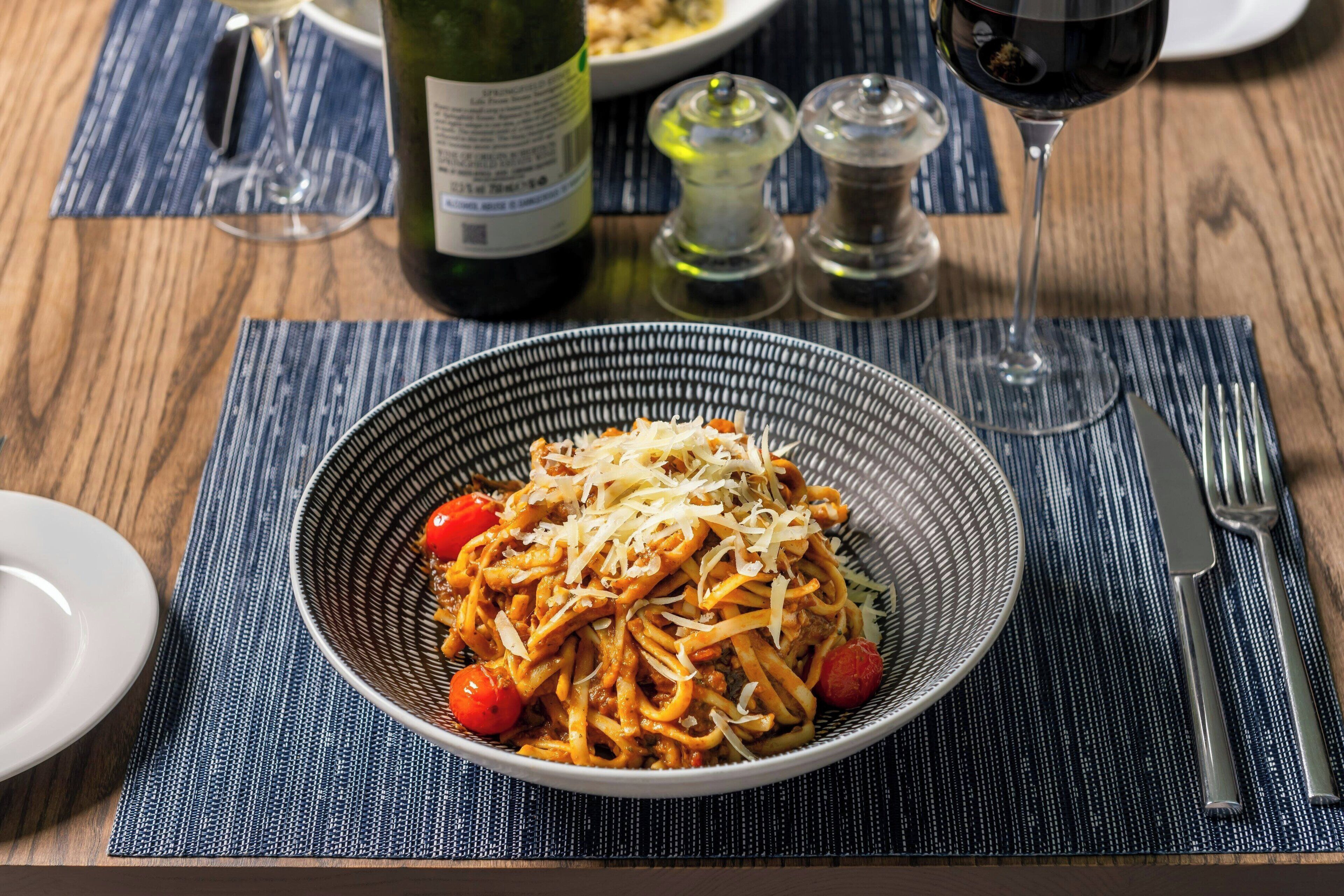 A bowl of spaghetti with cheese and cherry tomatoes on a blue placemat.