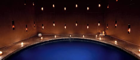 A large indoor swimming pool with a dark blue color, surrounded by walls with evenly spaced windows.