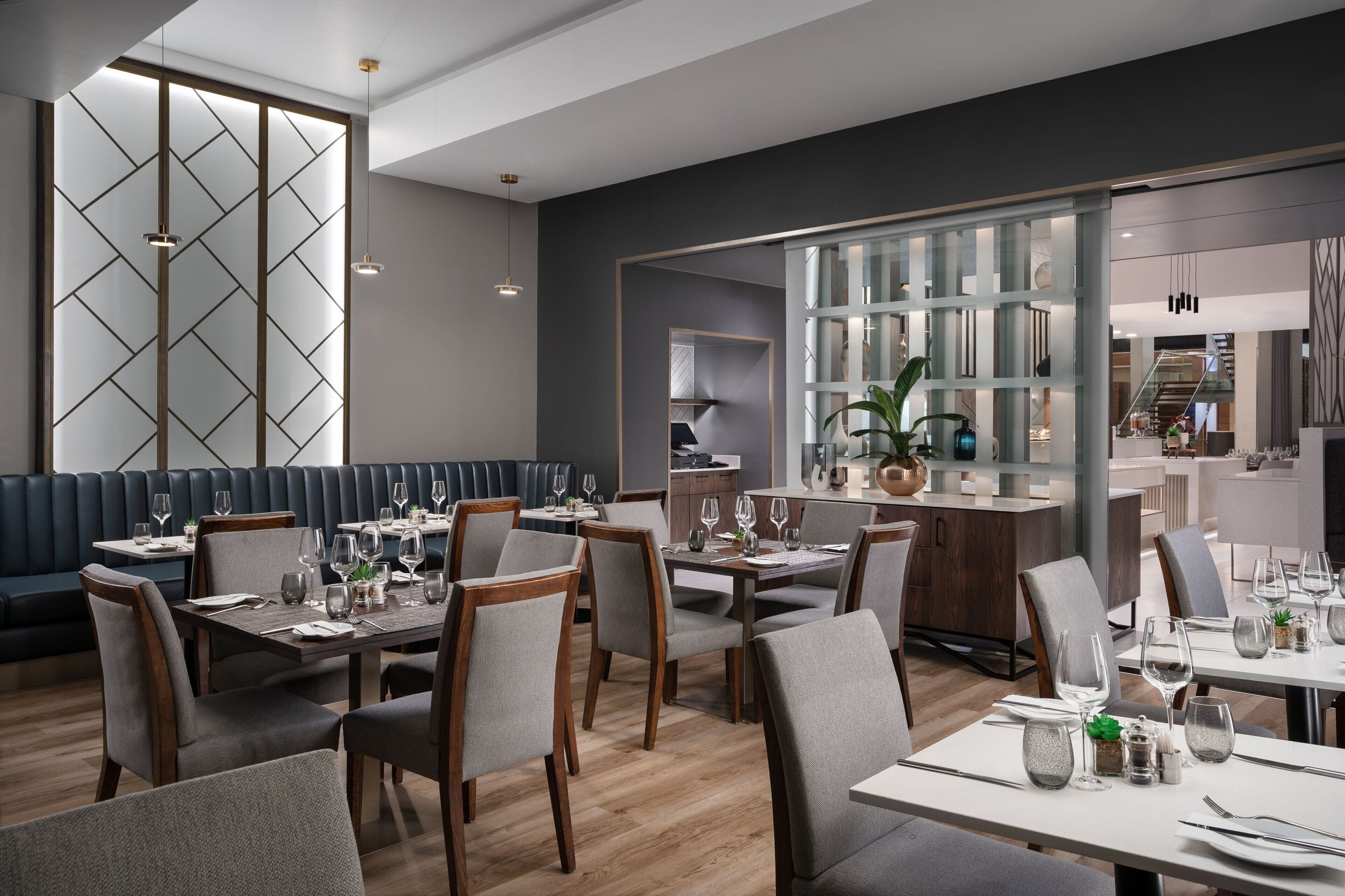 A modern restaurant with high tables and booths, wooden flooring, and a large glass partition separating the dining area from the kitchen.