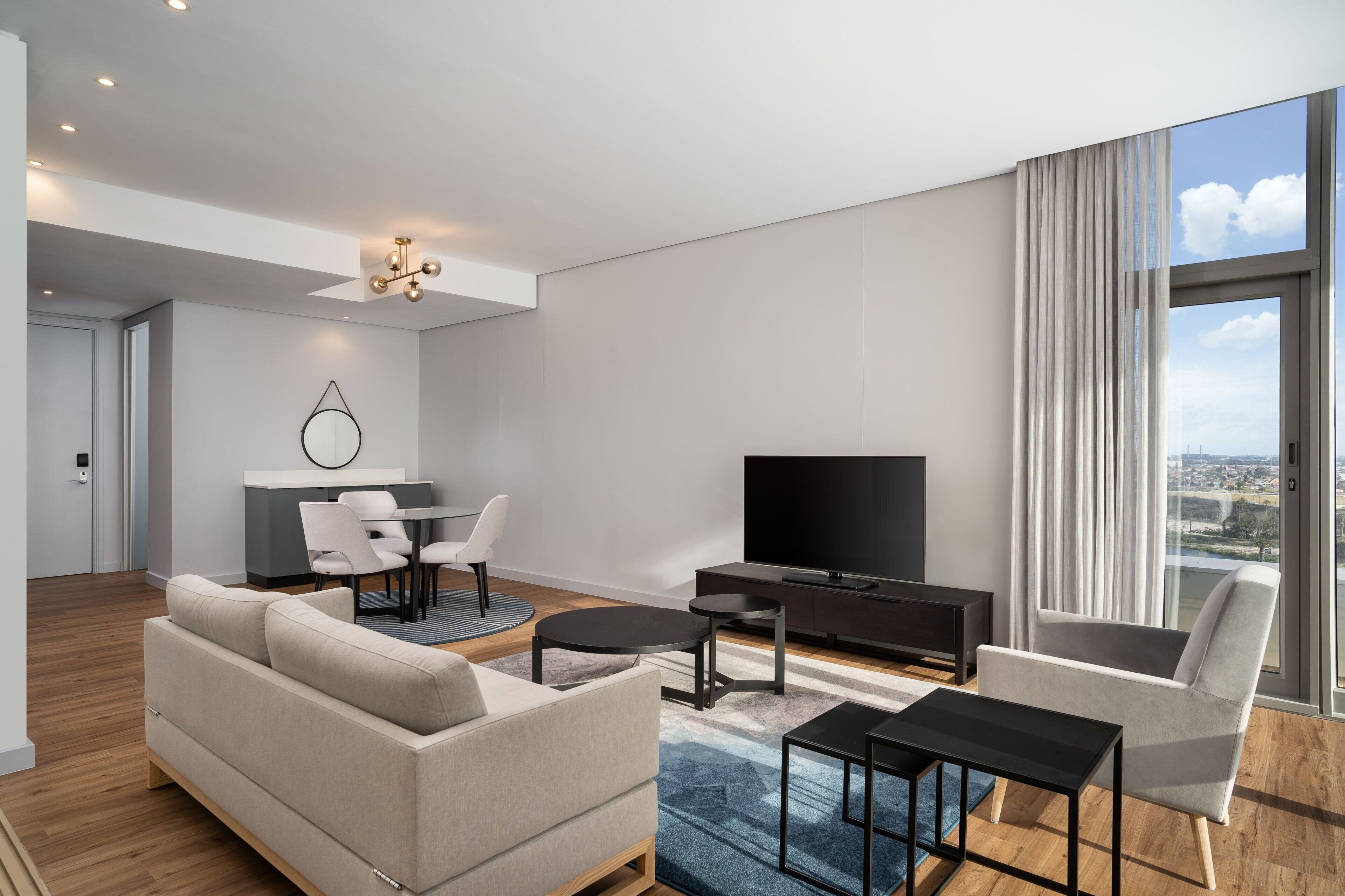 A modern living room with a sofa, coffee table, TV, and a dining area with chairs.