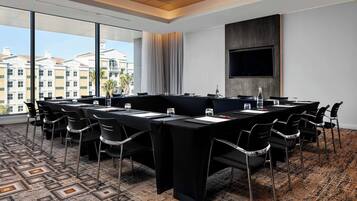 A conference room with a long table, chairs, a TV, and a large window with a city view.