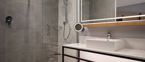 A modern bathroom with a glass-enclosed shower, a white sink, and a mirror with a wooden shelf above it.