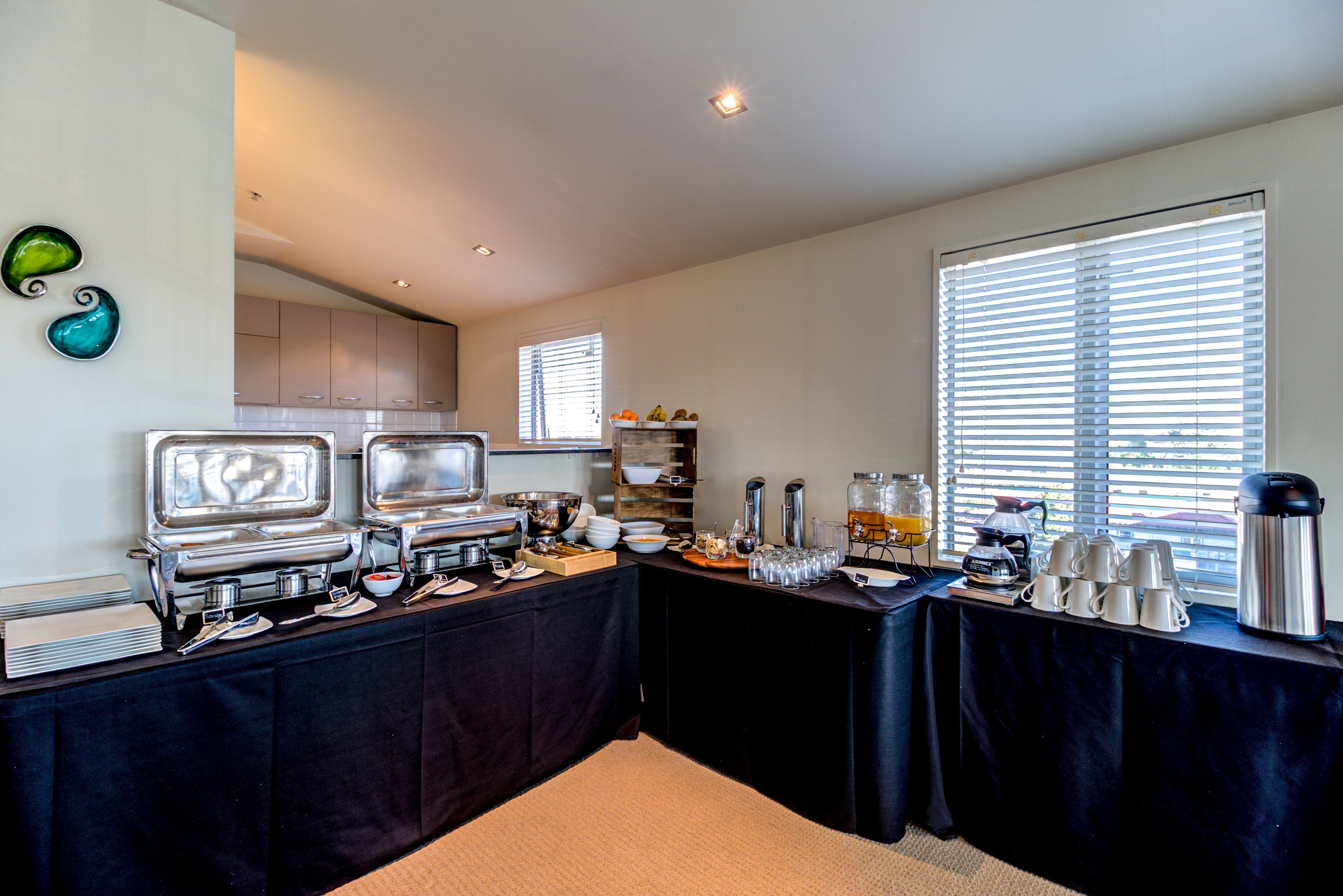 A buffet setup with multiple serving stations, a coffee maker, and a large window with blinds.