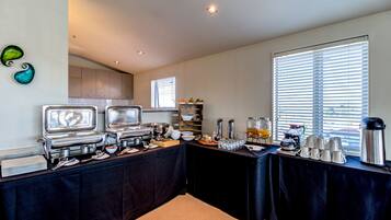 A buffet setup with multiple serving stations, a coffee maker, and a large window with blinds.