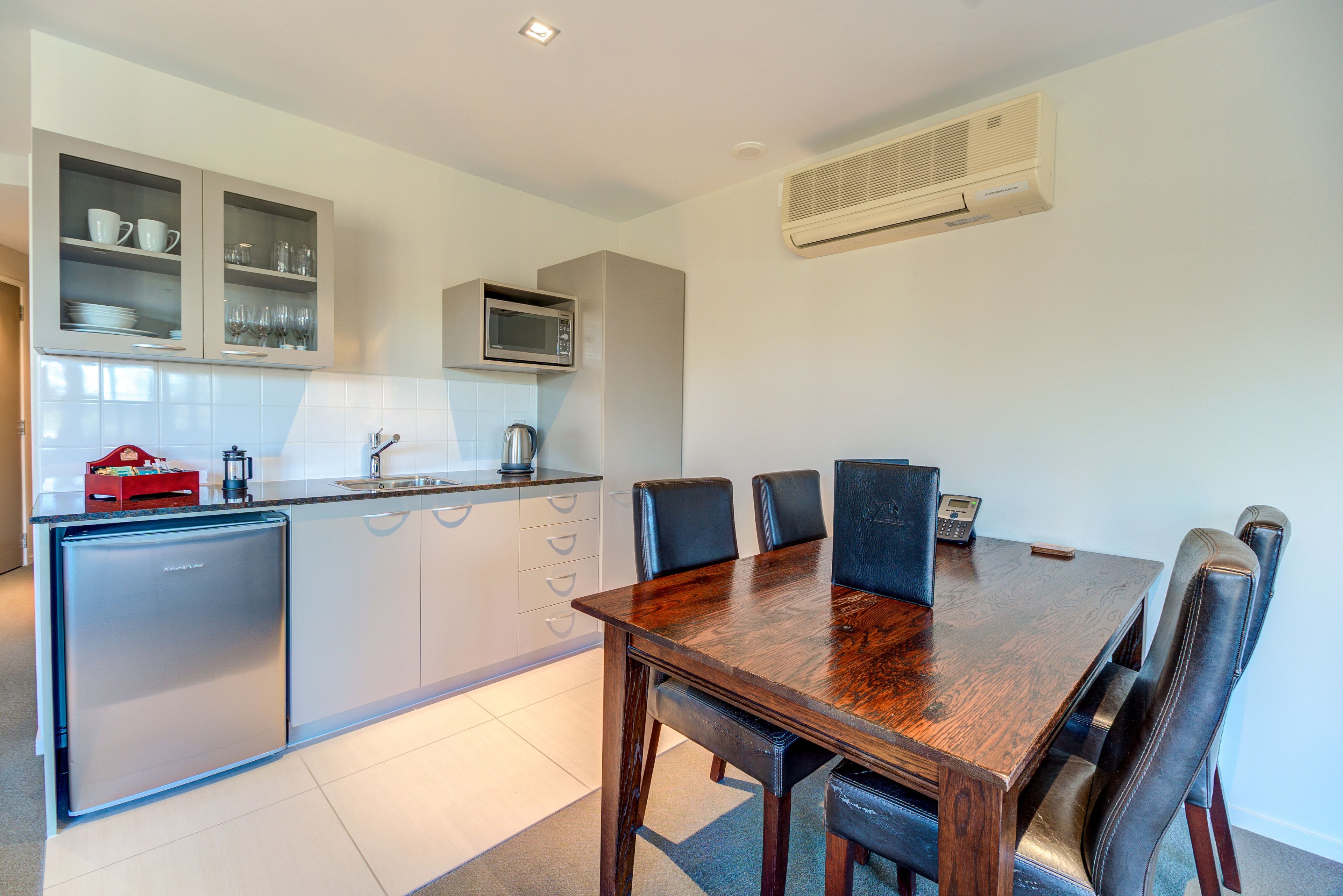 A modern kitchen with a built-in microwave, a refrigerator, and a dining area with a wooden table and chairs.