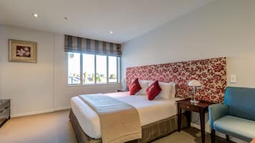 A bedroom with a large bed, a nightstand, a chair, a window with a view, and a floral-patterned headboard.