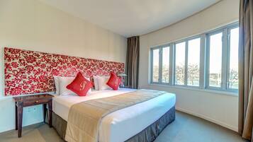 A bedroom with a large bed, a headboard with a floral pattern, and a window with curtains.