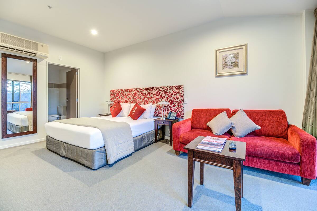 Une chambre d’hôtel avec un lit, un canapé rouge, une petite table et un miroir.