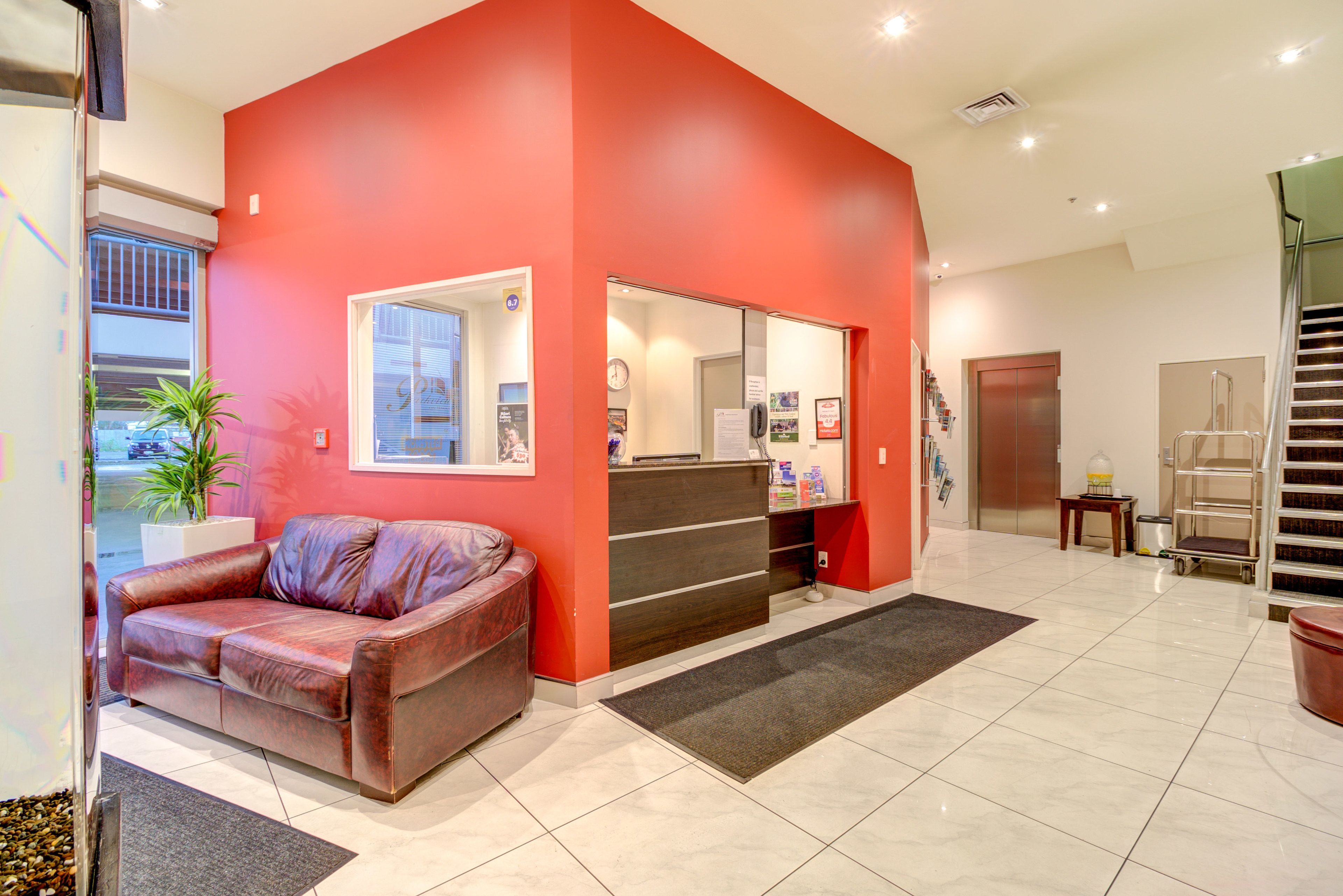 A reception area with a red wall, a leather sofa, a reception desk, a staircase, and a potted plant.