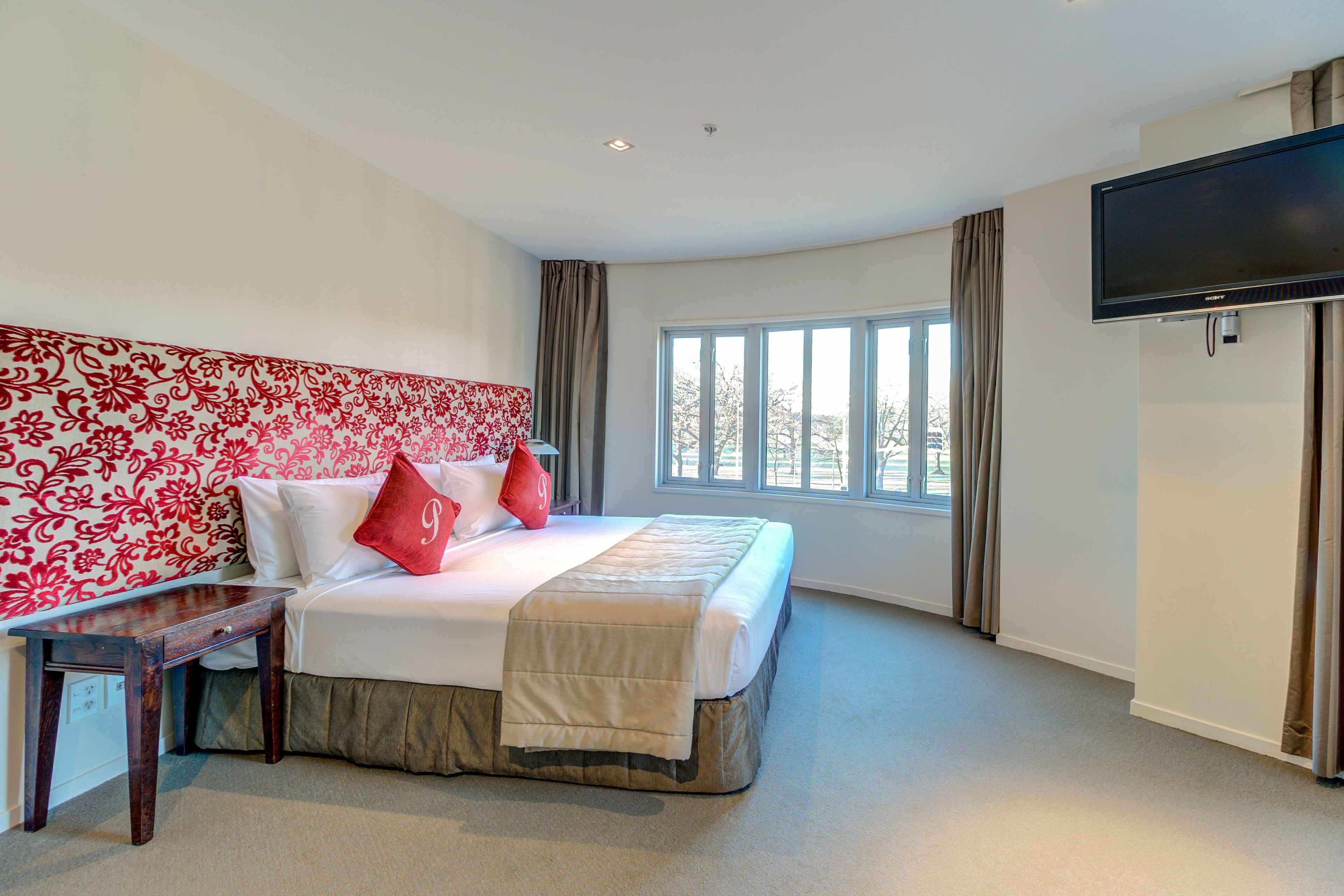 Une chambre d’hôtel avec un grand lit, un téléviseur fixé au mur et une fenêtre avec des rideaux.