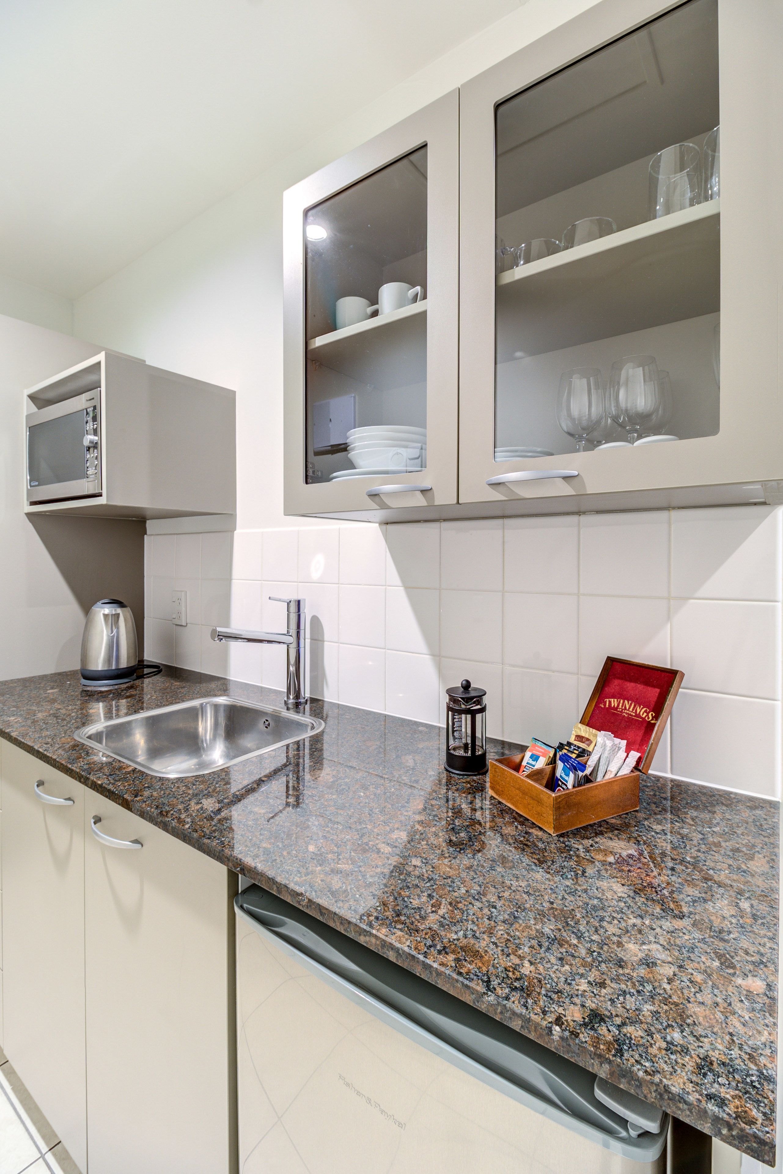 A kitchen with a granite countertop, stainless steel sink, and white cabinets.
