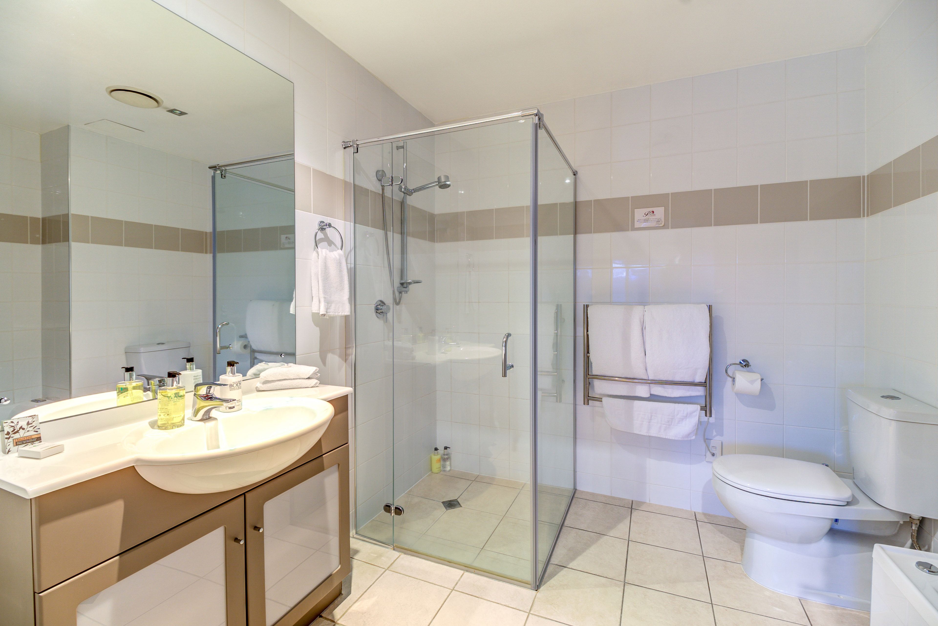 A modern bathroom with a glass-enclosed shower, a sink with toiletries, and a toilet.