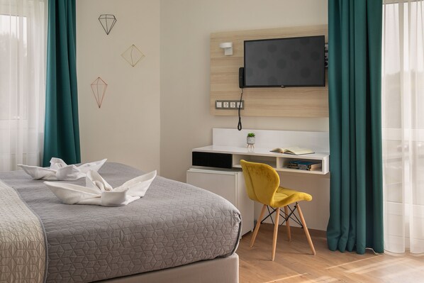 Una habitación de hotel con una cama, un escritorio con una computadora, un televisor y una silla.