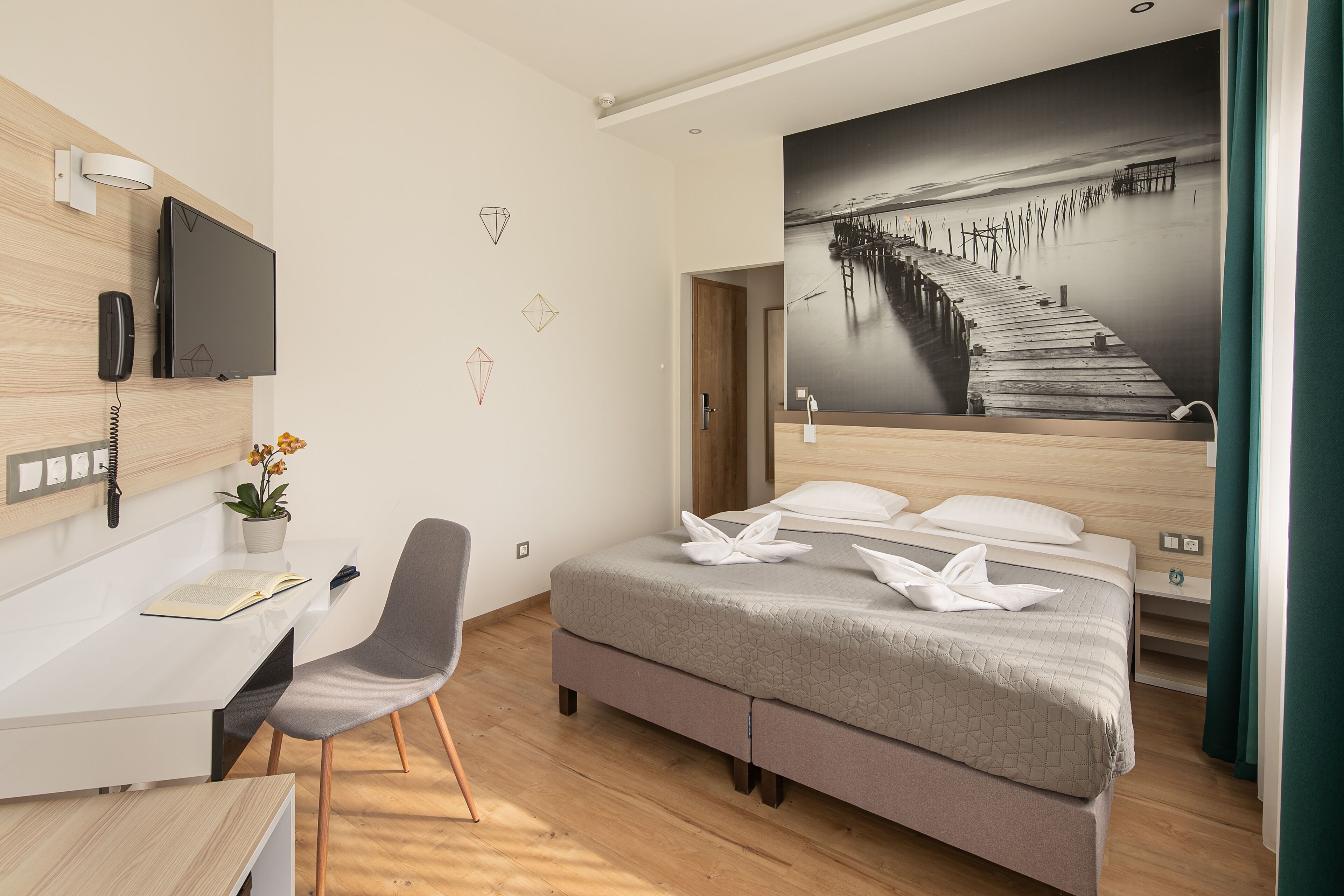A modern hotel room with a bed, desk, chair, and a large wall-mounted TV.