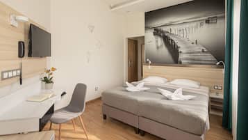 A modern hotel room with a bed, desk, chair, and a large wall-mounted TV.