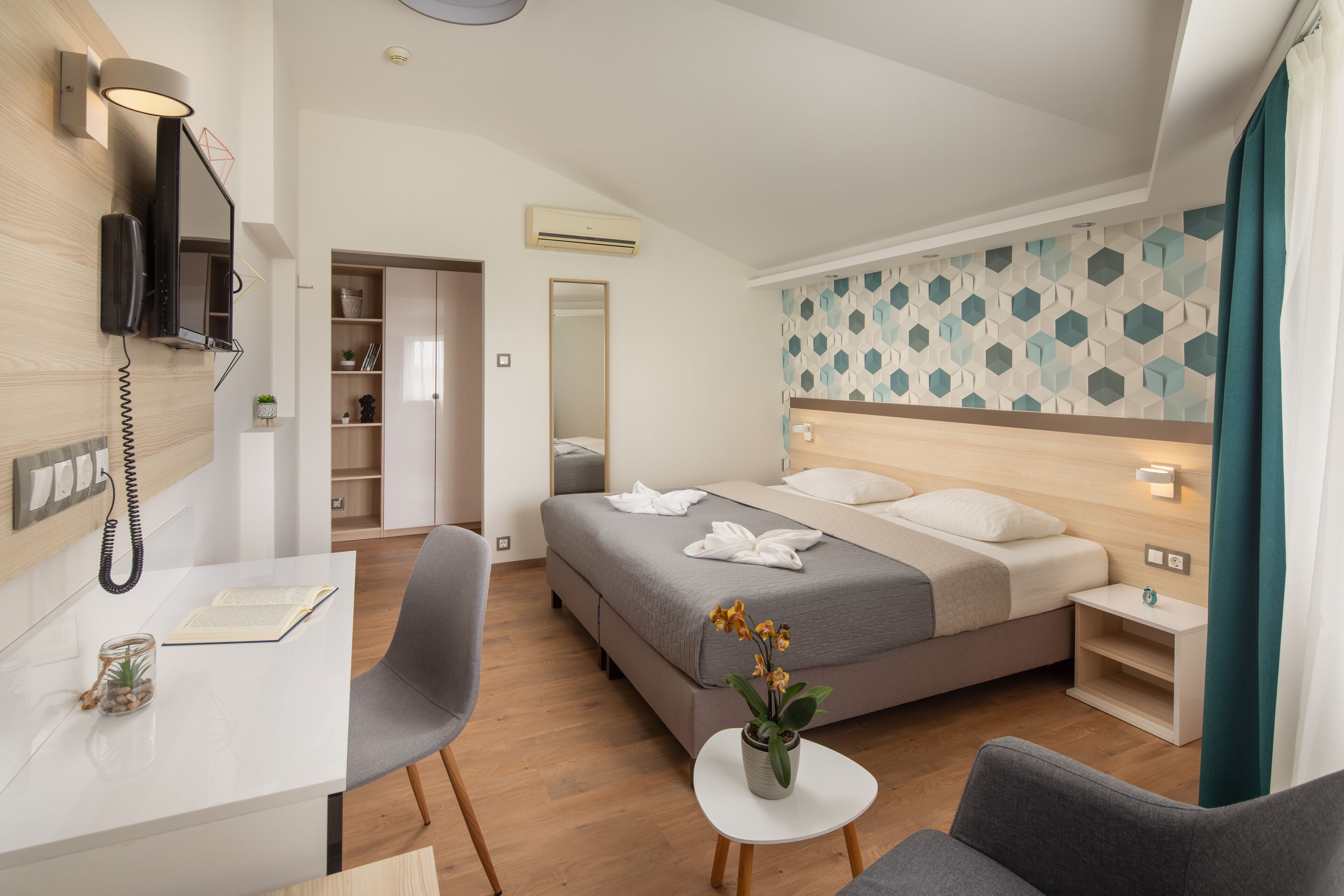 Une chambre d’hôtel moderne équipée d’un lit, d’un bureau, d’une chaise, d’une petite table avec un vase et d’un téléphone fixé au mur.