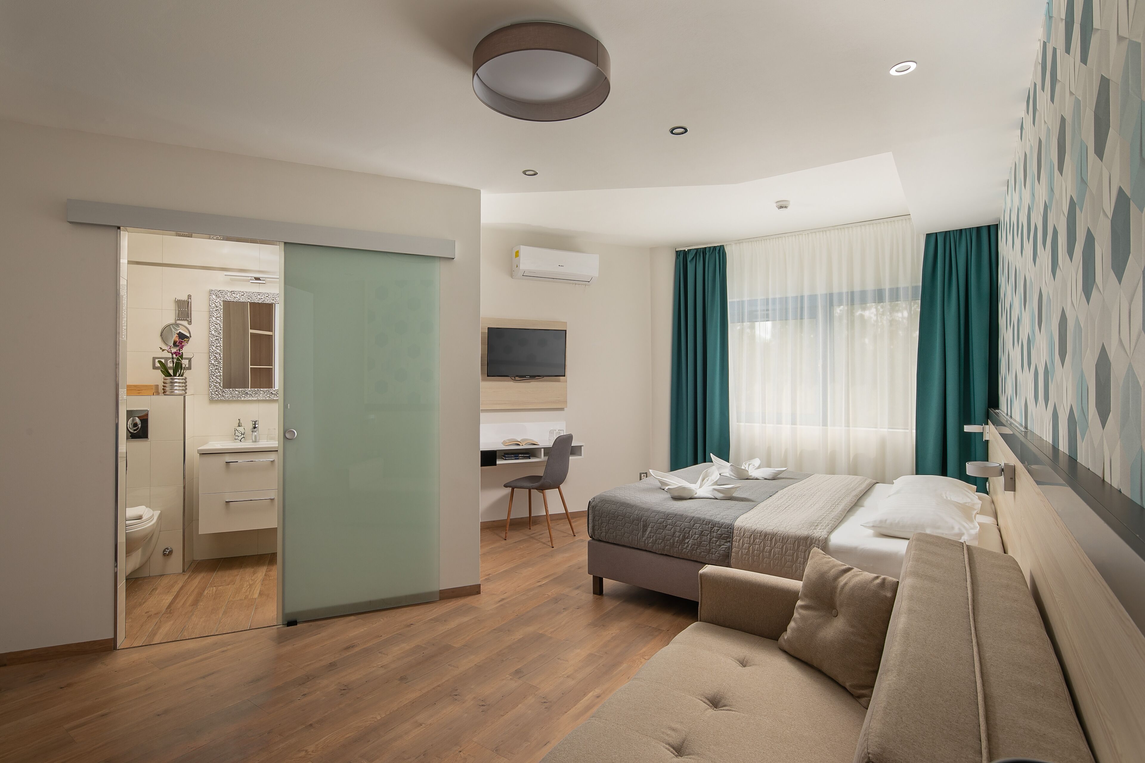 A modern hotel room with a bed, a sofa, a desk, and a bathroom.