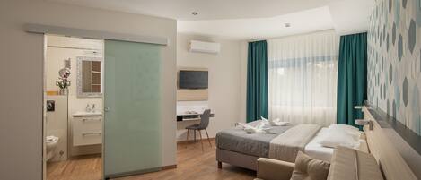 A modern hotel room with a bed, a sofa, a desk, and a bathroom.