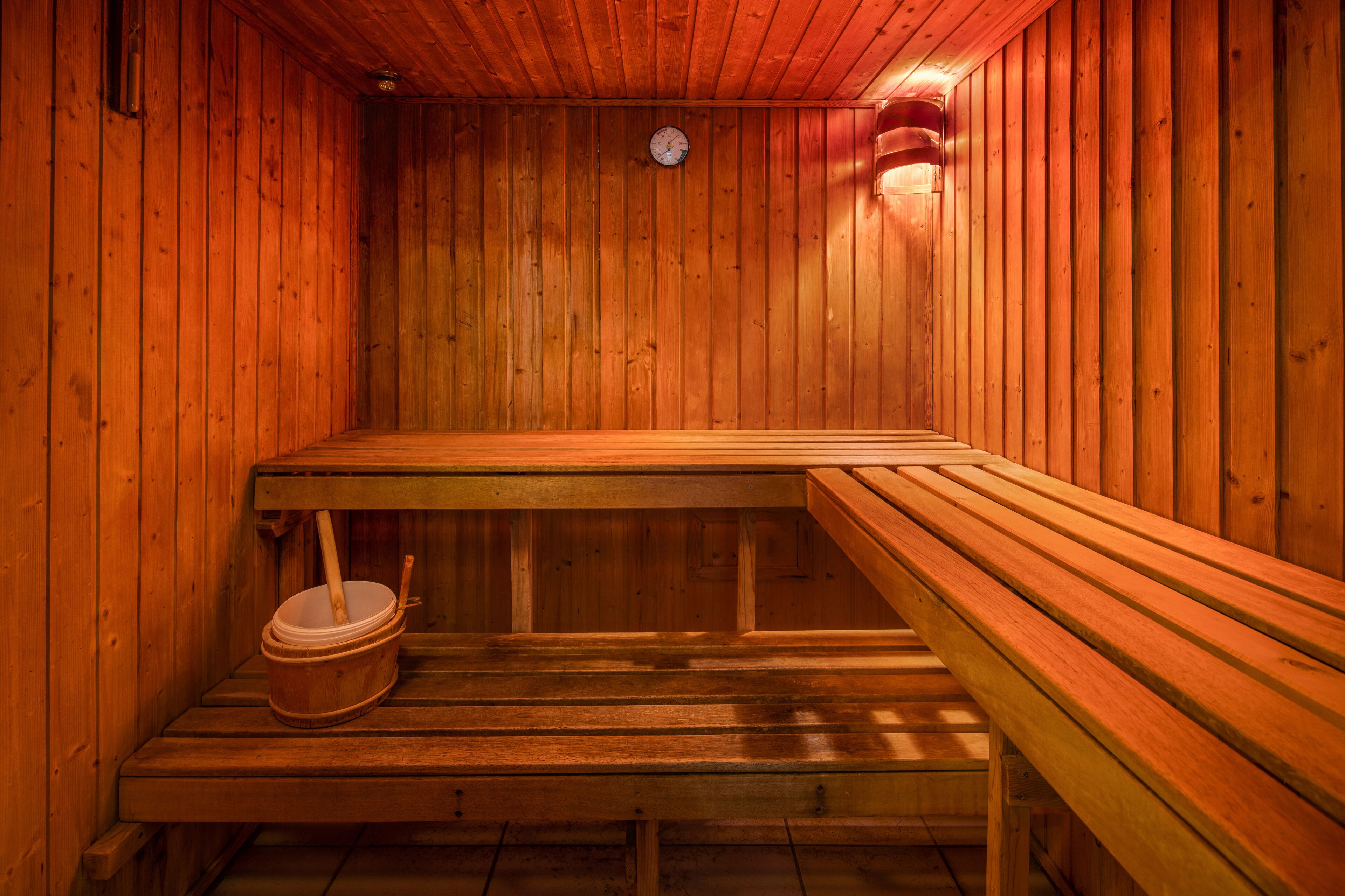 Una sauna amb seients de fusta i un cub de fusta.
