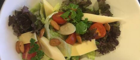 A white bowl containing a salad with lettuce, tomatoes, almonds, and cheese.