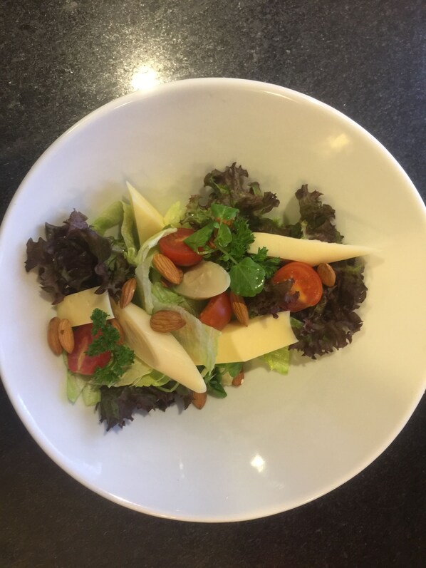 Un tazón blanco con ensalada de lechuga, tomates, almendras y queso.
