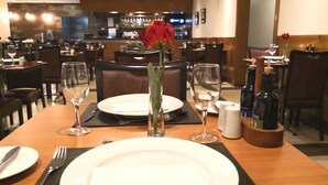 Een gedekte restauranttafel met borden, bestek, wijnglazen en een vaas met een rode roos.