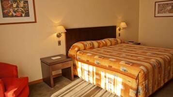 A hotel room with a large bed, a nightstand, a red chair, and two wall-mounted lamps.