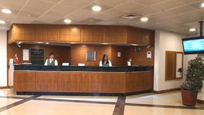 Een hotel receptiebalie met houten lambrisering, een scherm dat informatie toont, en een bloempot met plant.