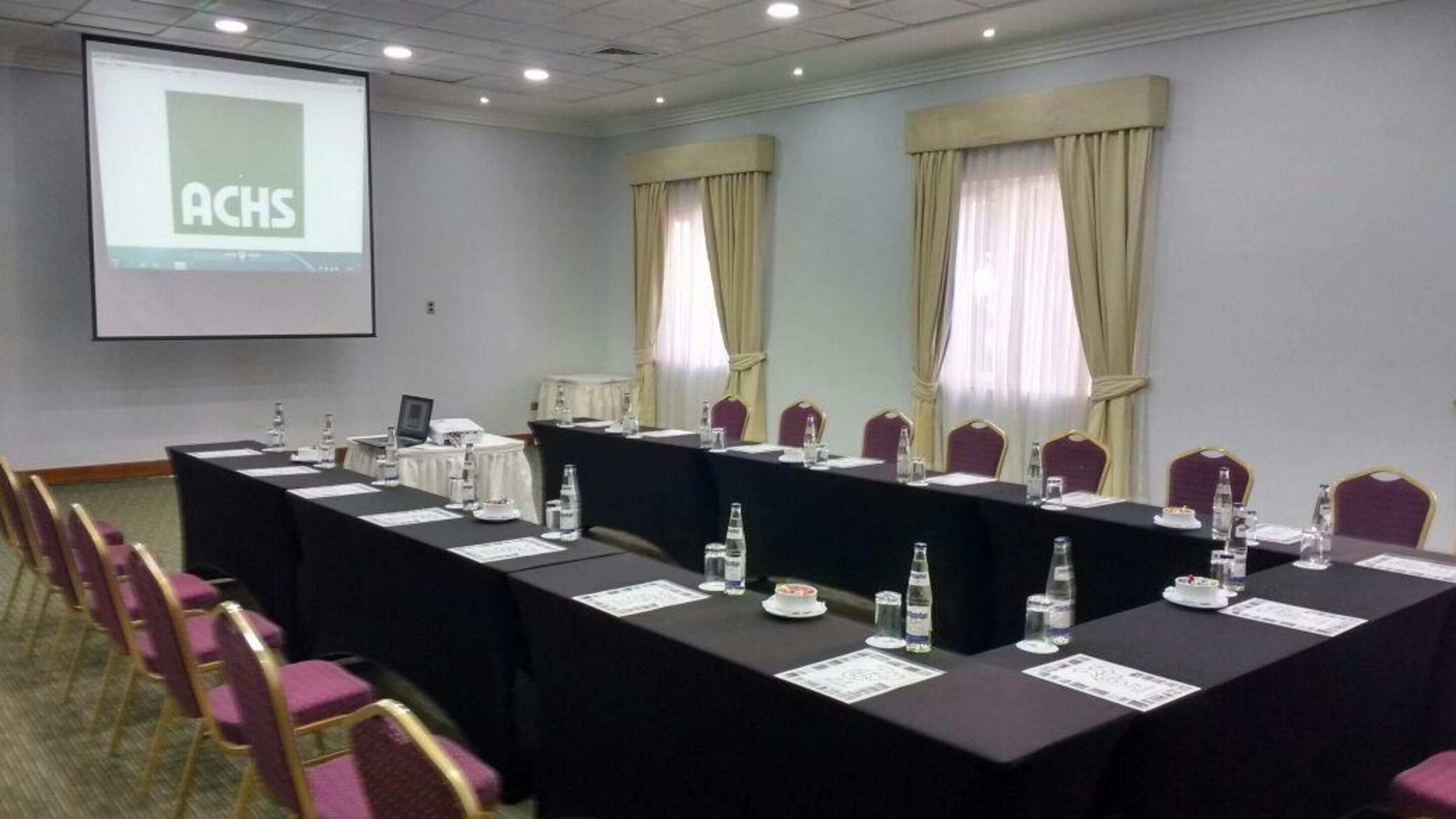 A conference room with a long table, chairs, and a projector screen displaying "ACHS".