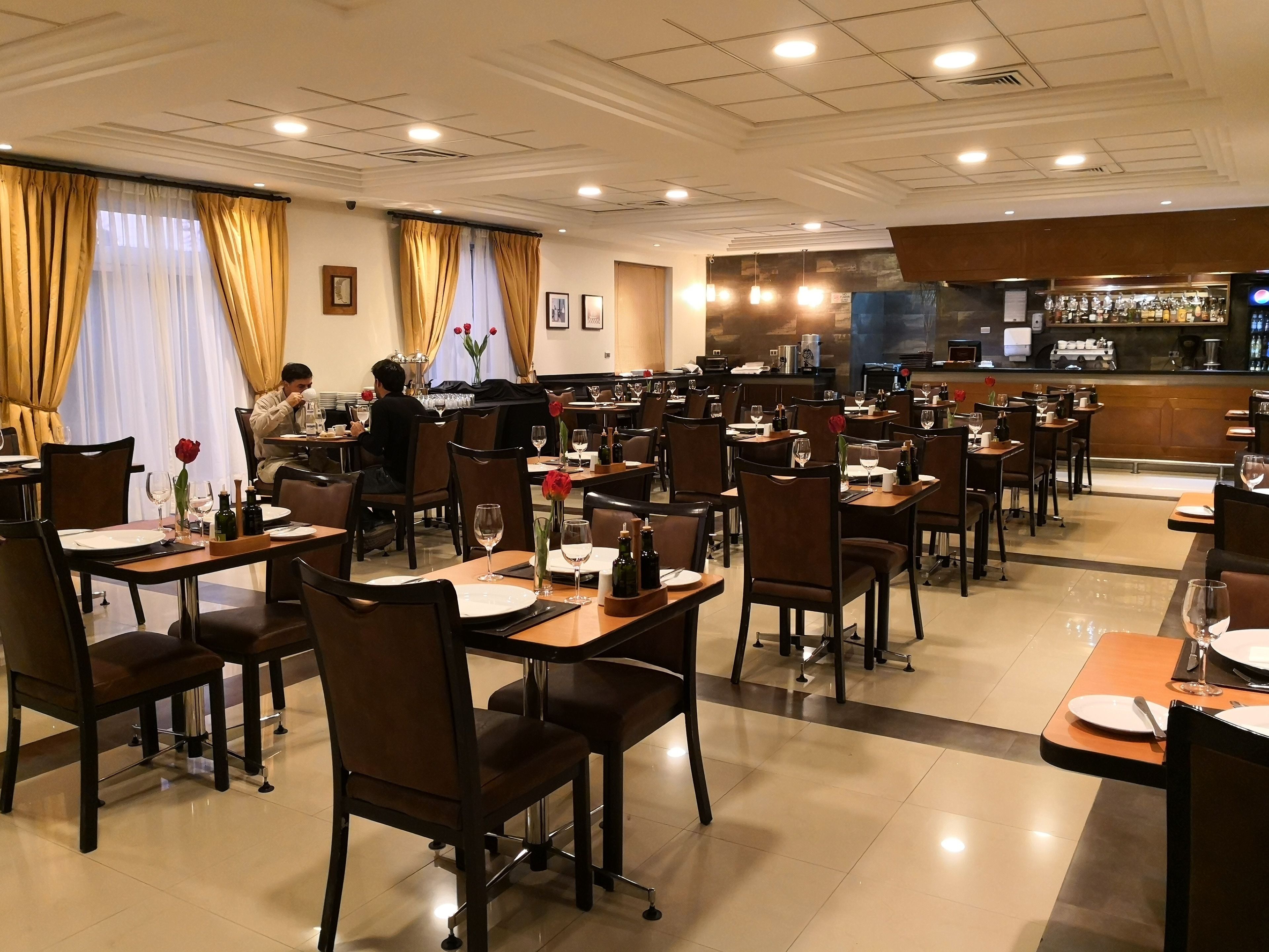 Un restaurante con varias mesas y sillas, una zona de bar e iluminación empotrada en el techo.