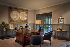 A spacious office with a large desk, two chairs, a globe map, and a window with a view of greenery.