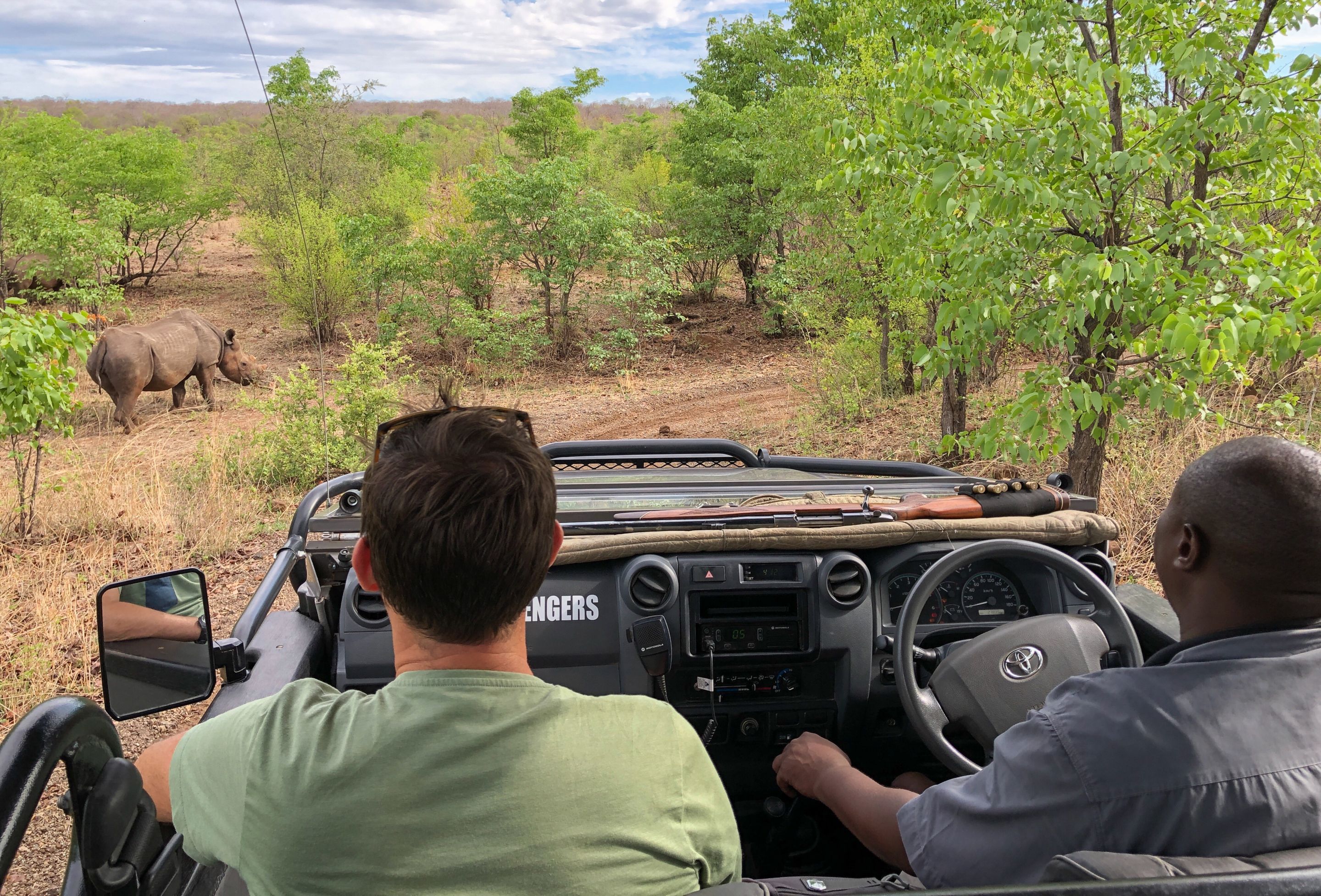 A safari vehicle with two occupants, a man driving and another man in the passenger seat, observing wildlife in a natural setting.