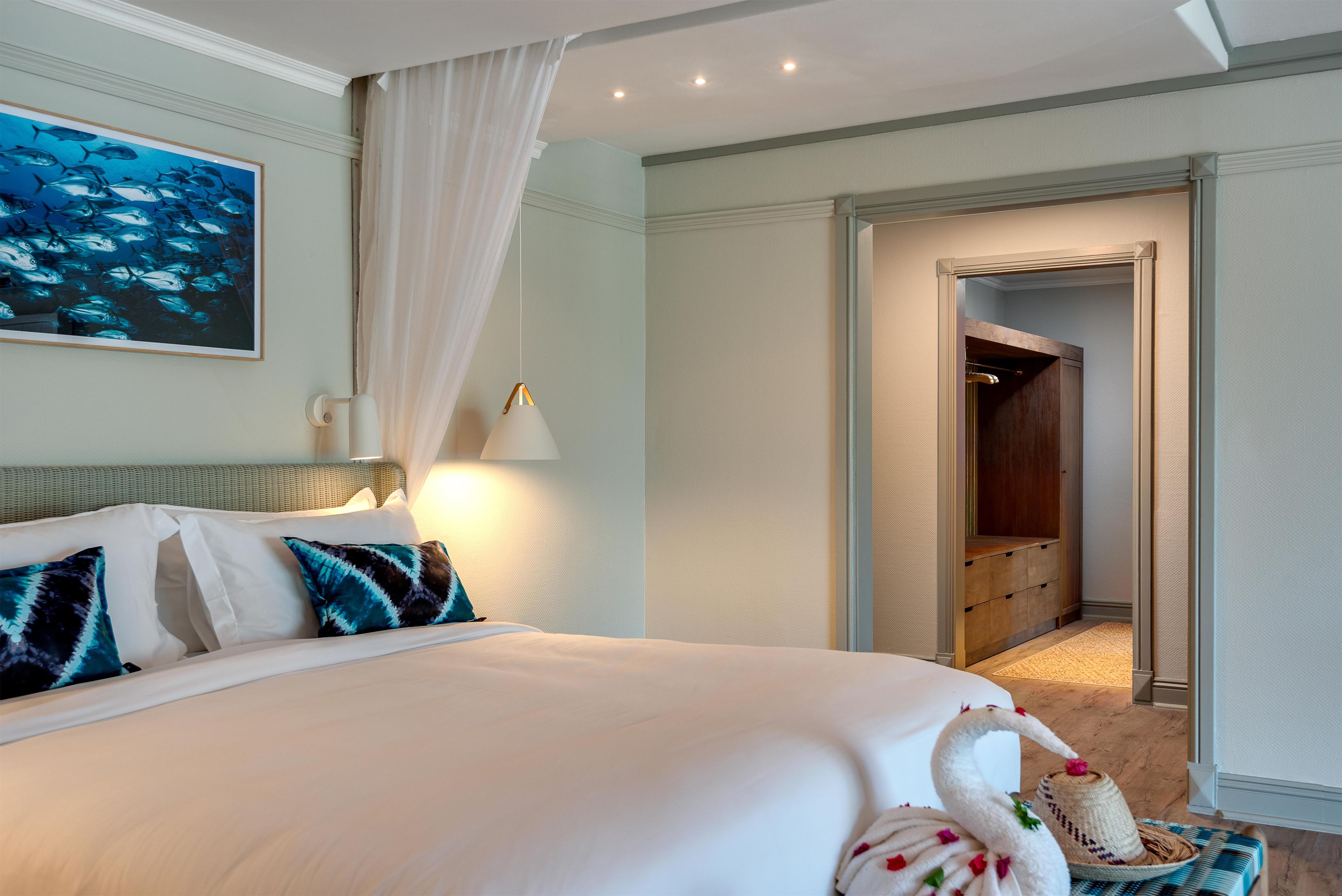 A hotel room with a large bed, a painting of fish on the wall, a bedside lamp, and a wooden wardrobe.