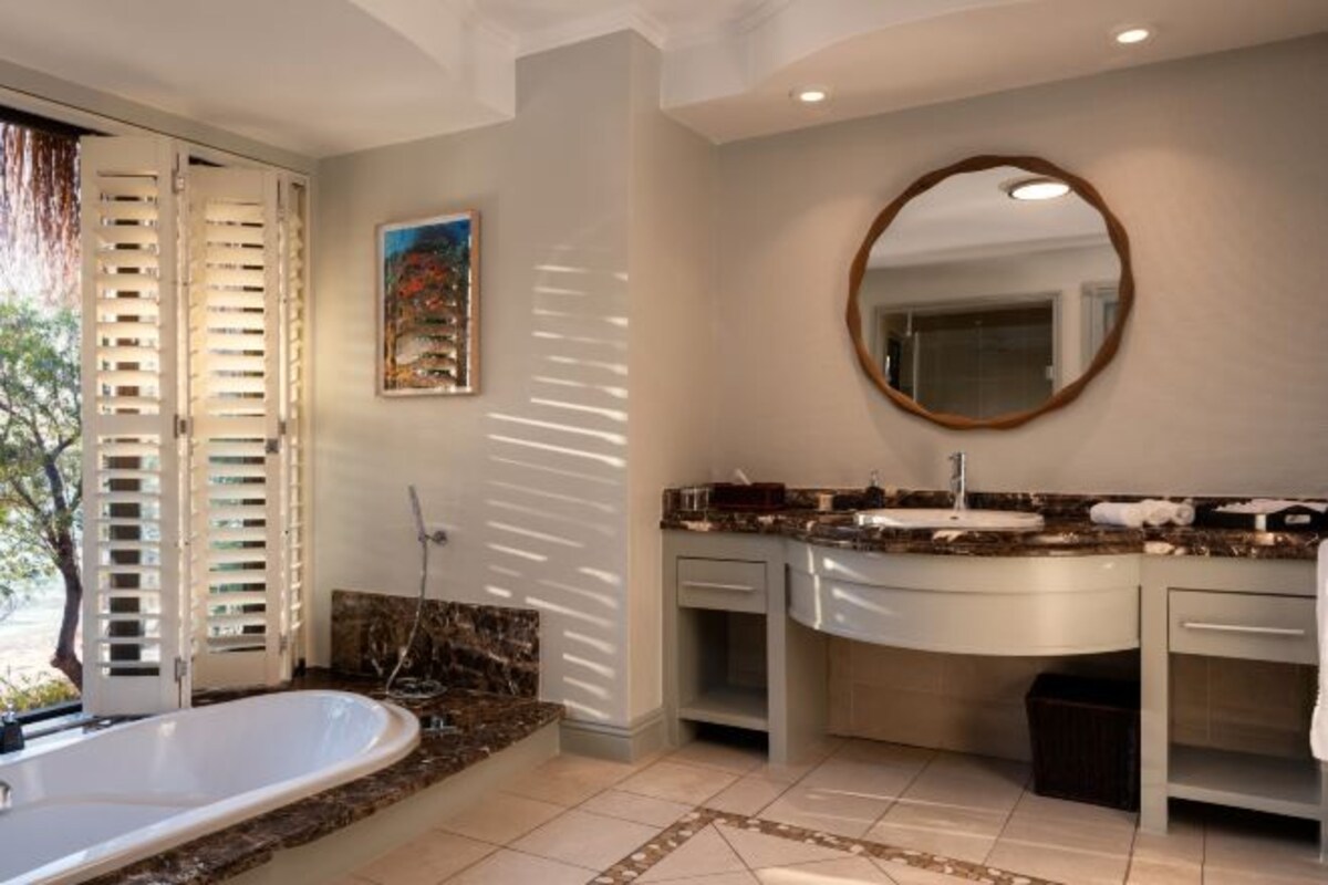 Une salle de bain avec une baignoire, deux lavabos, un miroir et une douche.