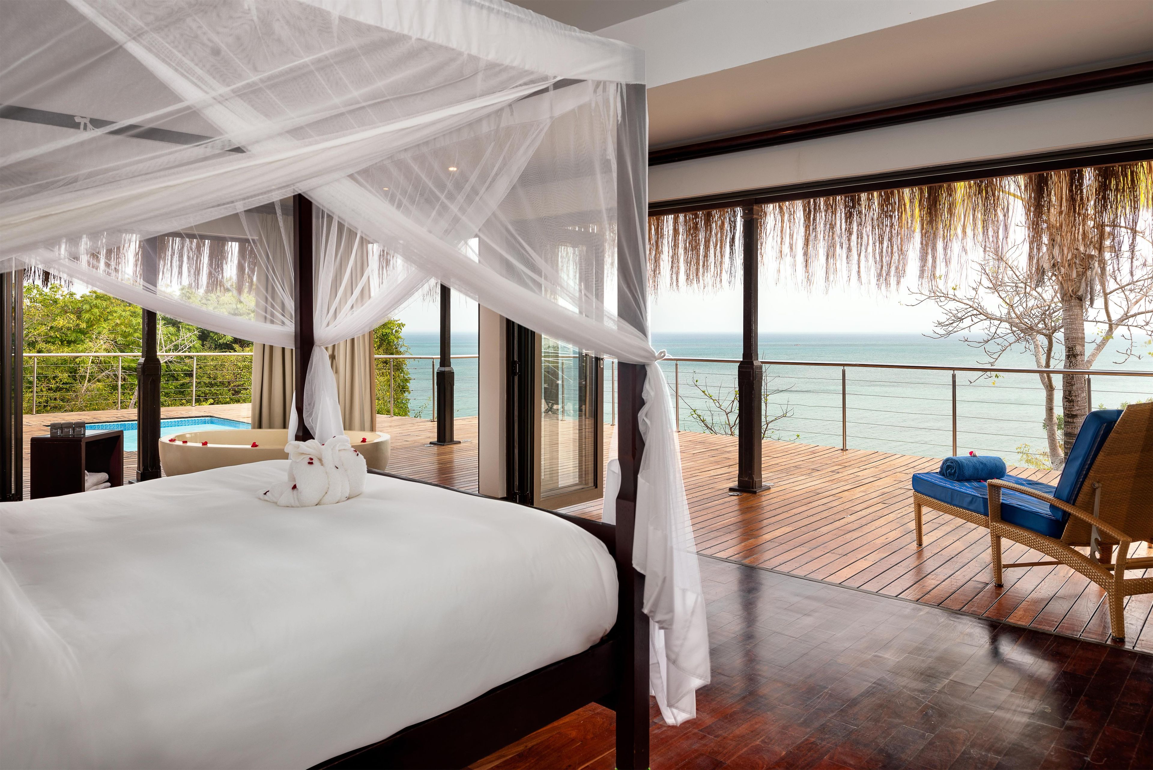 Un dormitorio con cama a dosel, vista al mar y terraza de madera con una silla.
