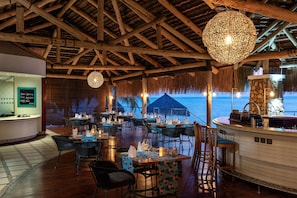 Un espace de restauration intérieur avec des poutres en bois, des tables dressées pour le dîner et une vue sur la mer.