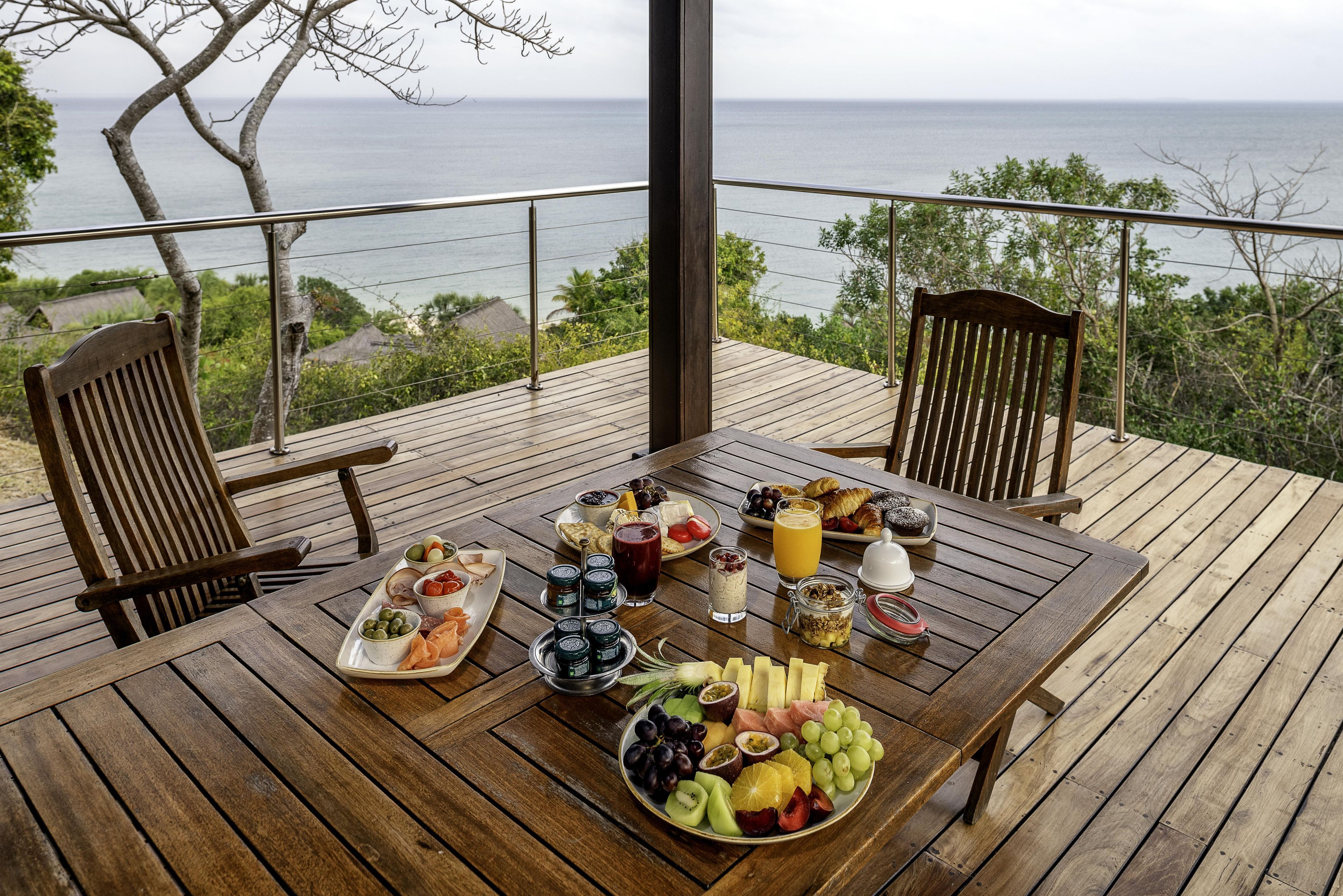 Una terraza de madera con una mesa lista para el desayuno, con vista a un cuerpo de agua.