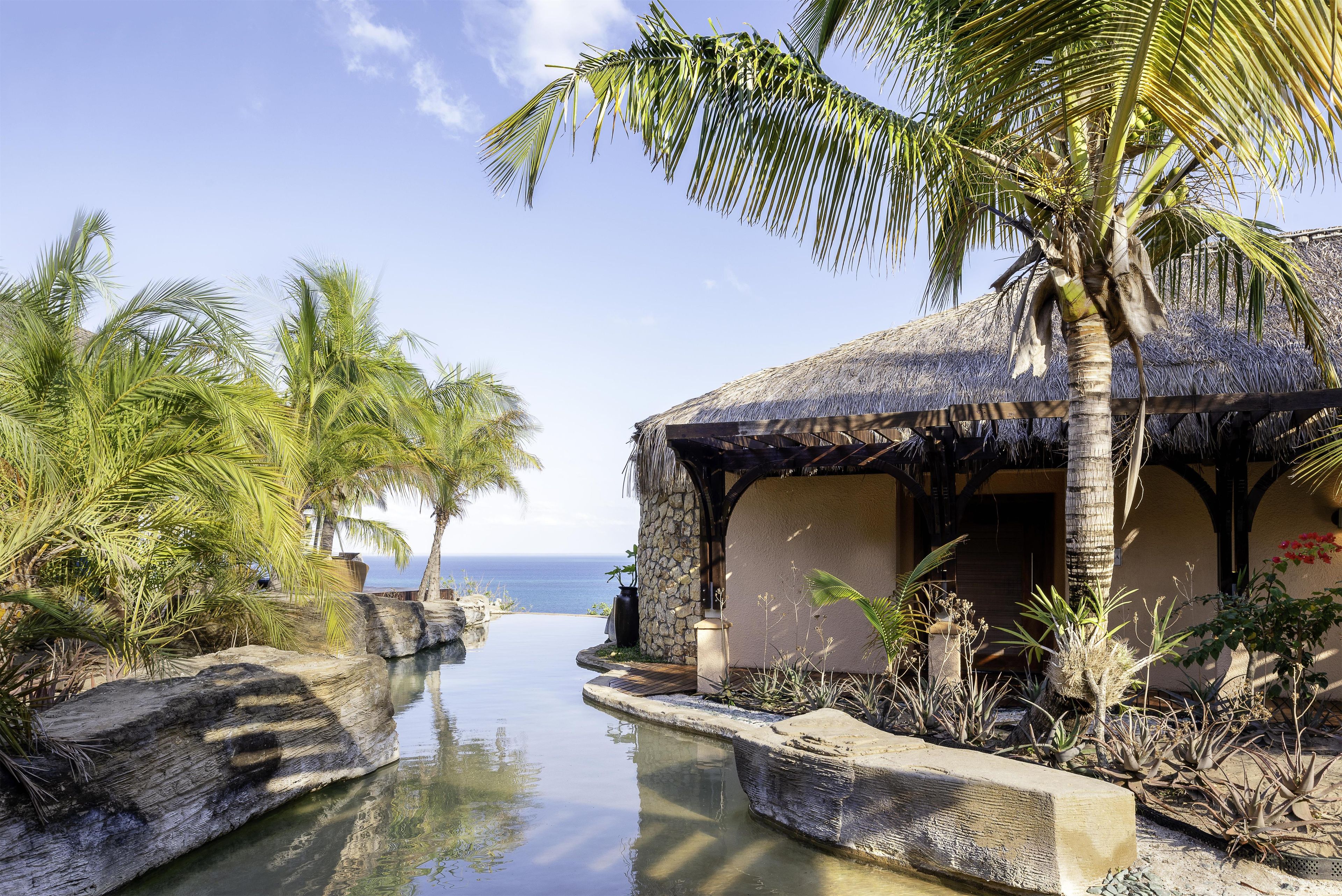 A tropical resort with a pool, palm trees, and a view of the ocean.
