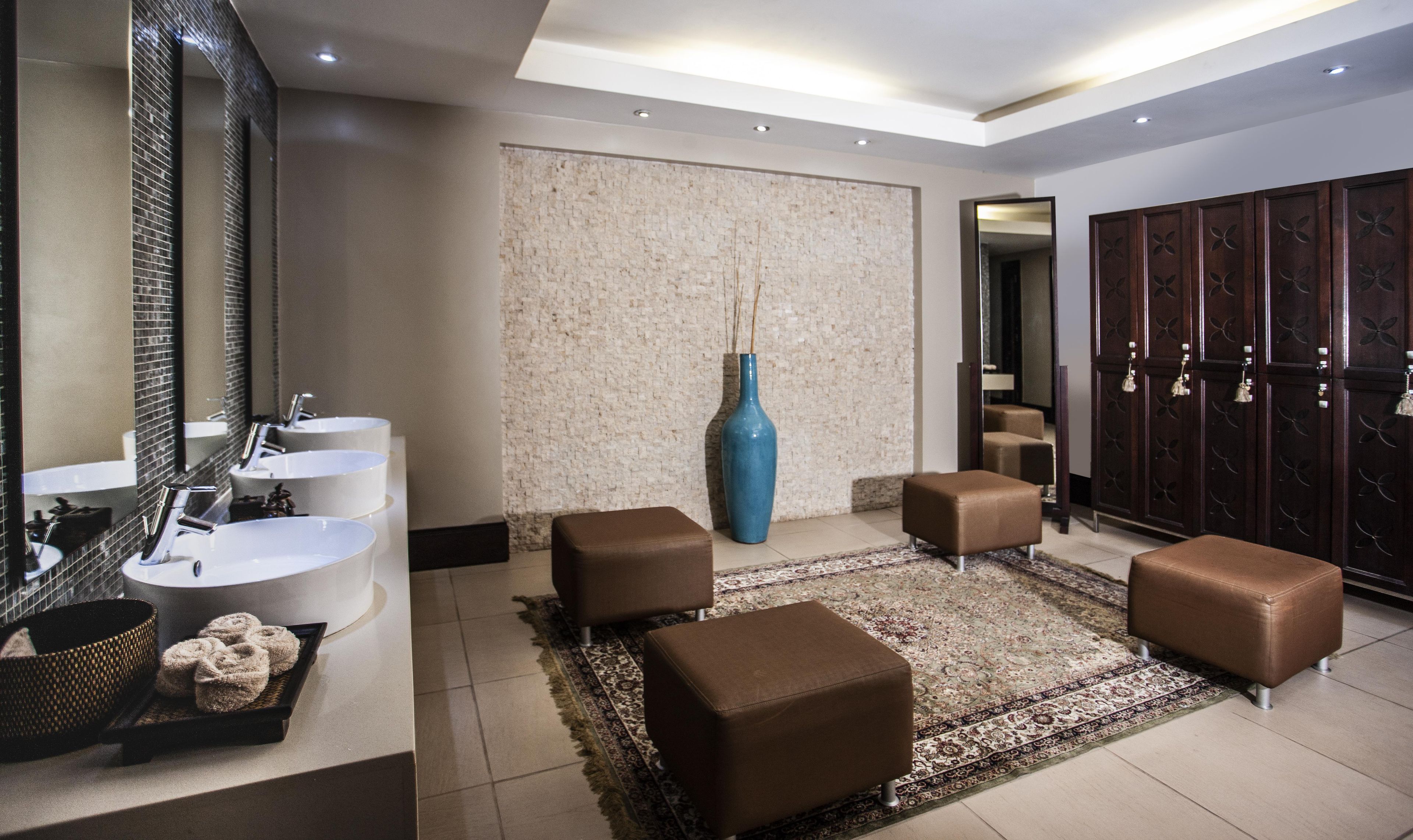 Une salle de bain moderne avec deux vasques, un grand miroir, un vase bleu et un tapis à motifs.