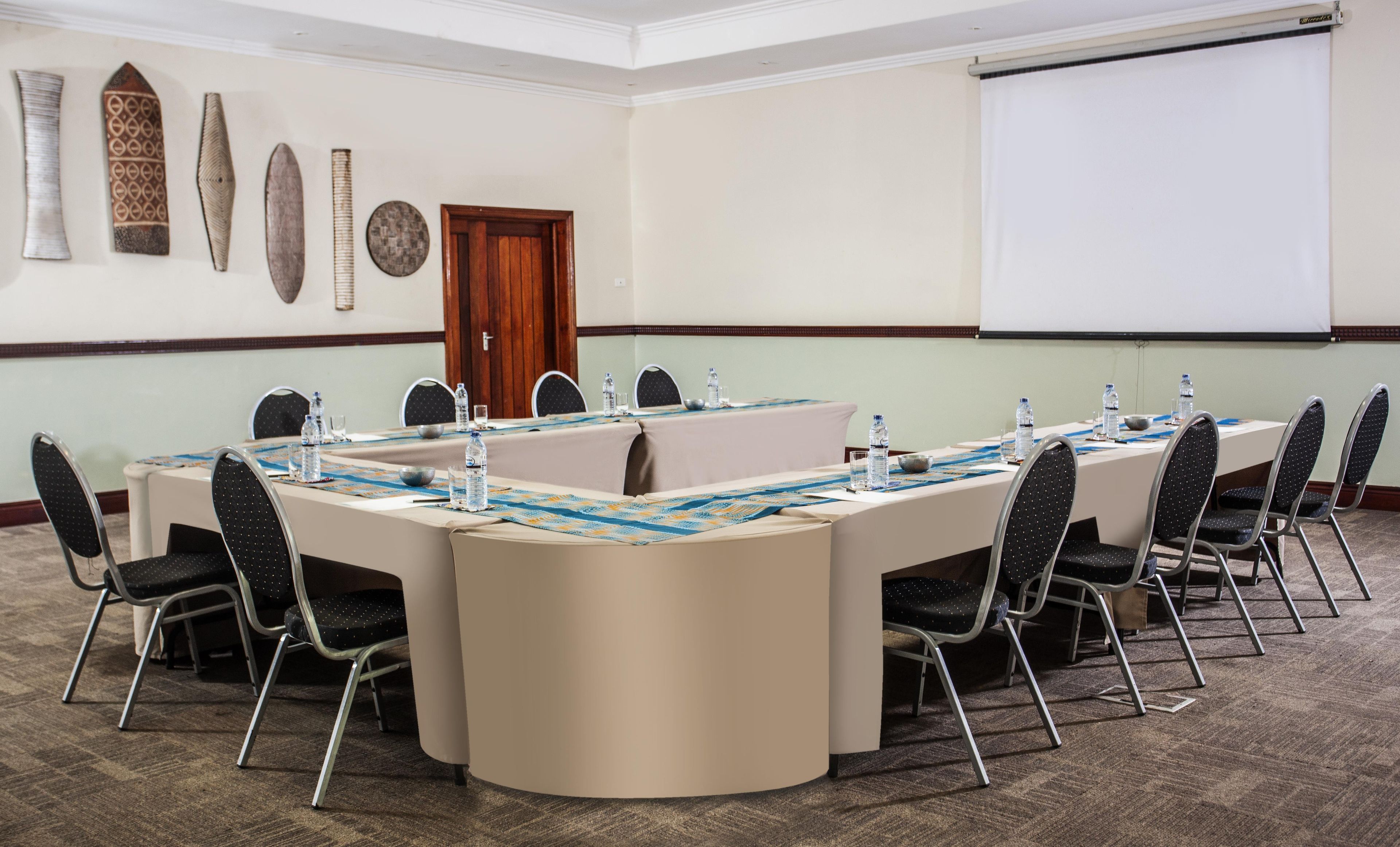 A conference room with a long table, chairs, a projector screen, and decorative wall art.