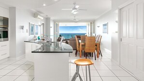 Una cocina moderna con una isla central, un comedor con sillas de mimbre y vista al mar.