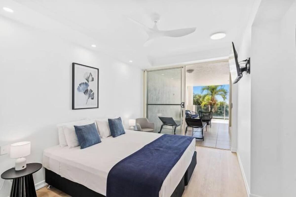 Une chambre moderne avec un grand lit, un ventilateur de plafond et une vue sur la terrasse extérieure.