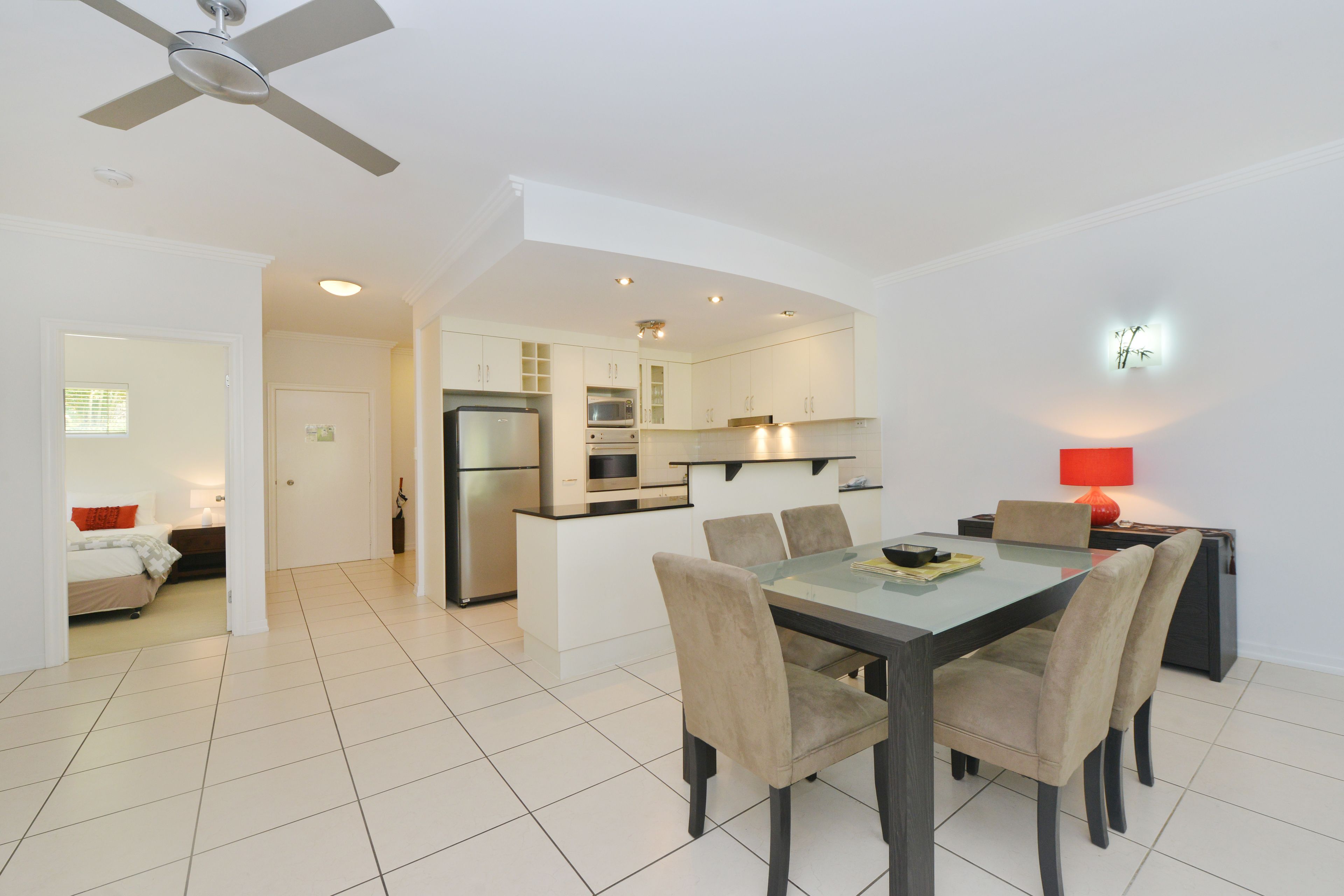 Una cocina moderna con zona de comedor, que incluye una mesa de vidrio, sillas color beige y un ventilador de techo.