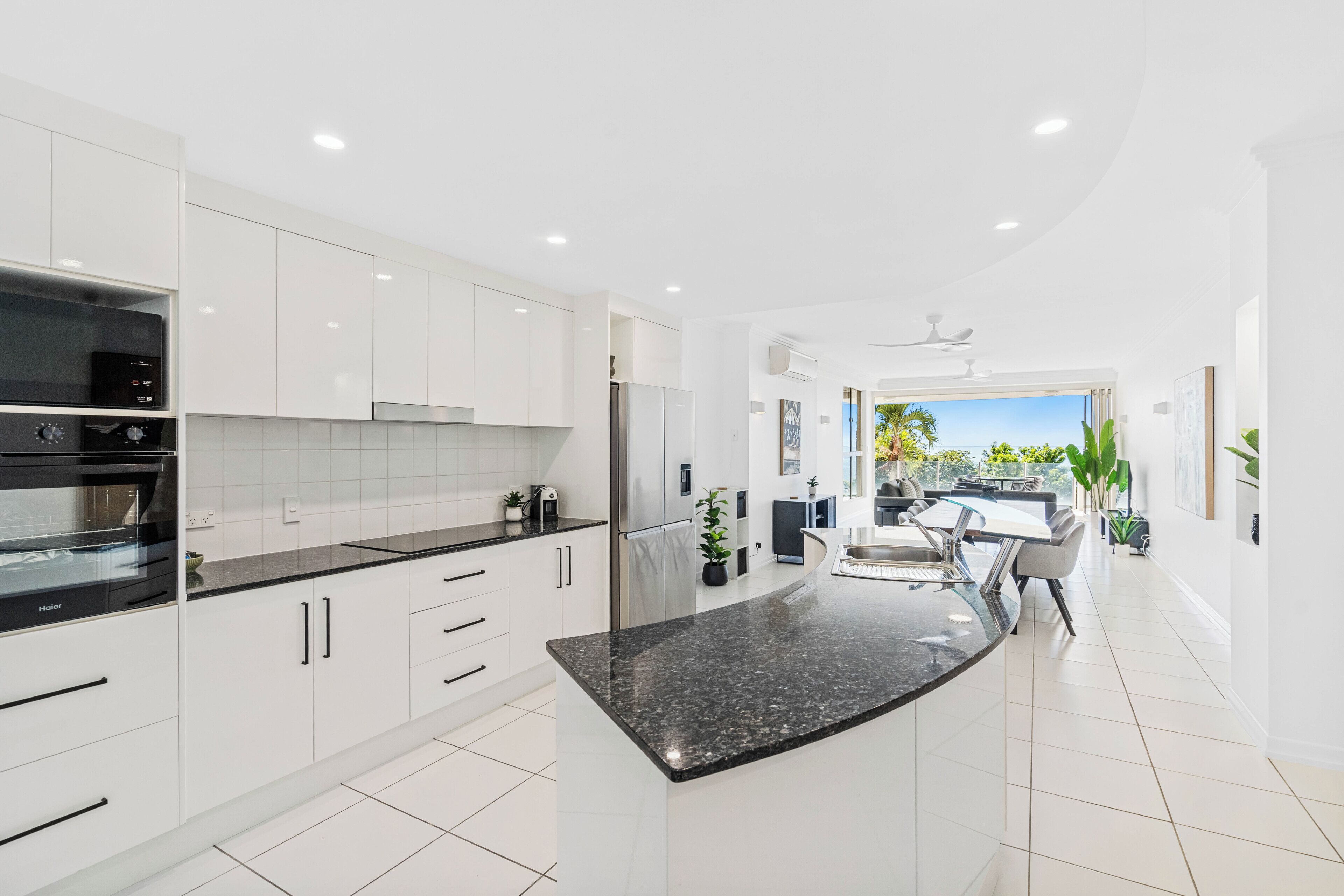 Une cuisine moderne avec des meubles blancs, un plan de travail en granit noir et un coin repas comprenant une table et des chaises.