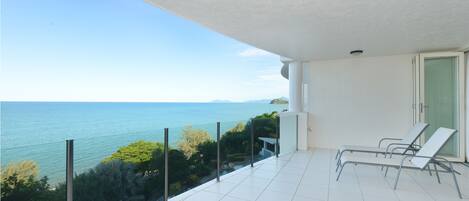 Un balcon avec vue sur la mer, un sol carrelé de couleur blanche et deux fauteuils de relaxation.